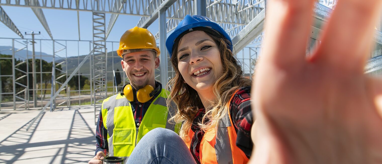 Ein Handwerker und eine Handwerkerin machen ein Selfie auf einer Baustelle.