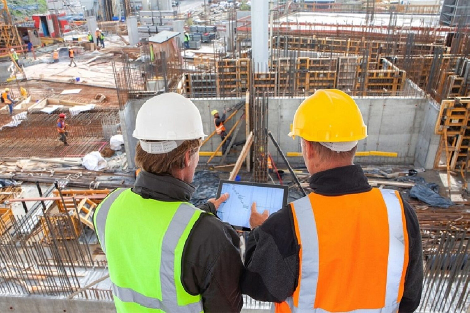 Handwerker mit Tablet-PC auf einer großen Baustelle.