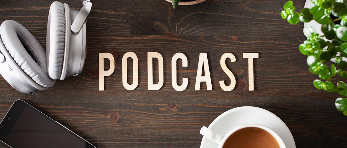 Tisch mit Schrift "Podcast" und einem iPhone, Kaffee, Kopfhörern.