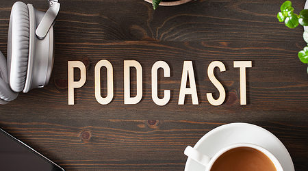 Tisch mit Schrift "Podcast" und einem iPhone, Kaffee, Kopfhörern.