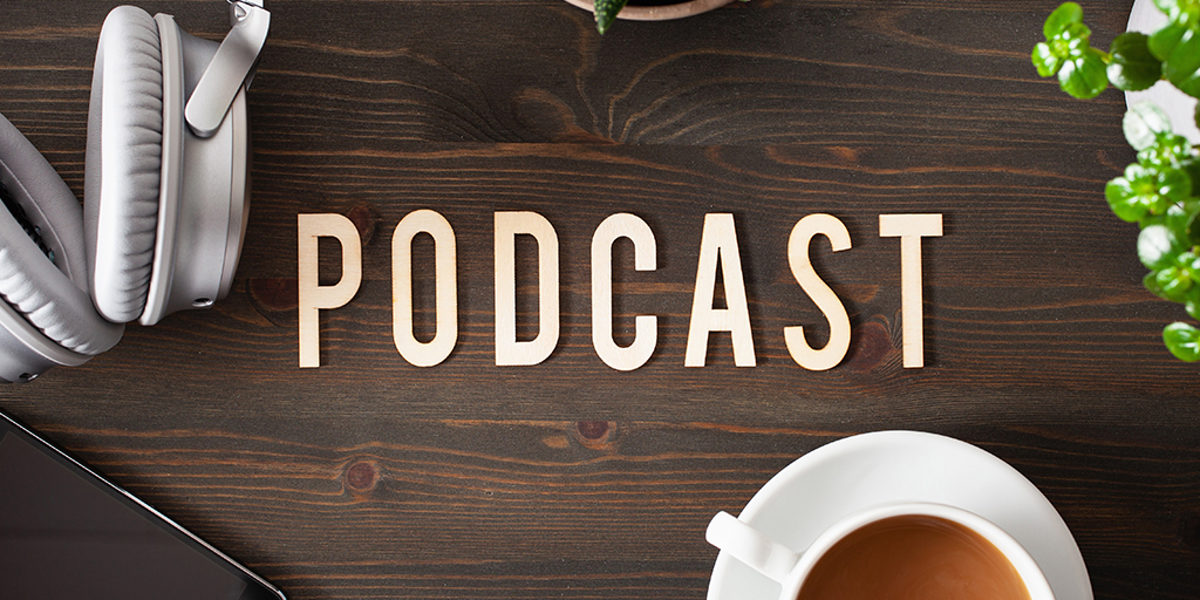 Tisch mit Schrift "Podcast" und einem iPhone, Kaffee, Kopfhörern.