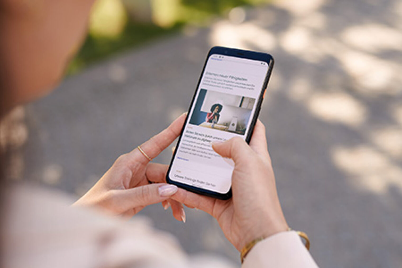 Eine Frau läuft mit einem Smartphone auf einem Weg entlang und liest dabei einen Artikel der Handwerkskammer Berlin. 