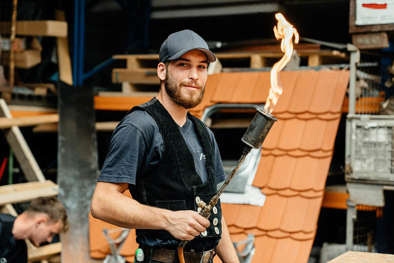 Ein Dachdecker-Azubi mit einer Fackel in der Hand auf dem Dach