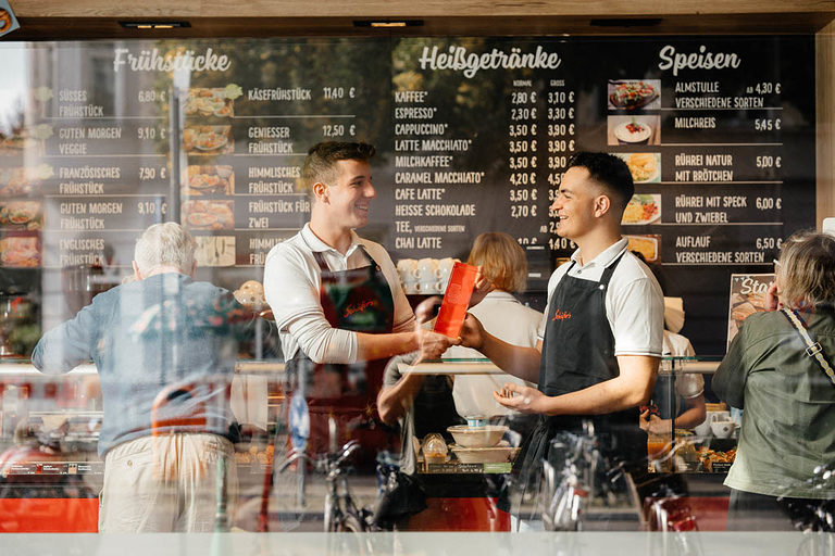 Zwei Verkäufer-Azubis in einem Café lächeln einander an