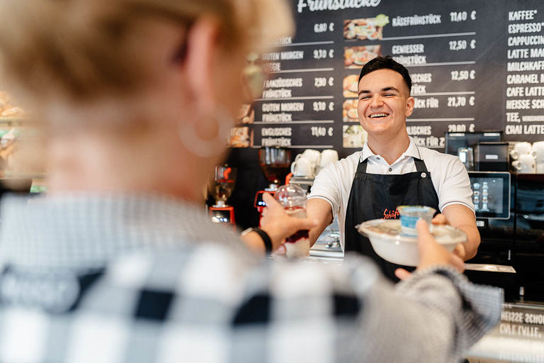 Ein Verkäufer-Azubi beim Reichen der Speisen am Tresen in einem Café