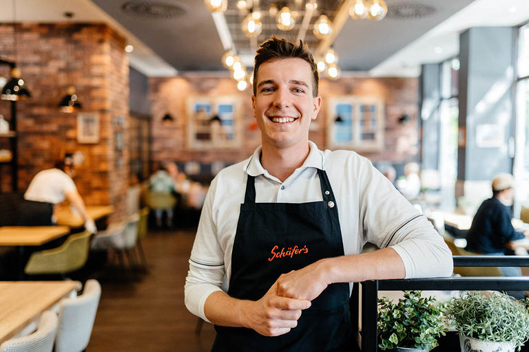 Ein Verkäufer-Azubis posiert lächelnd in einem Café