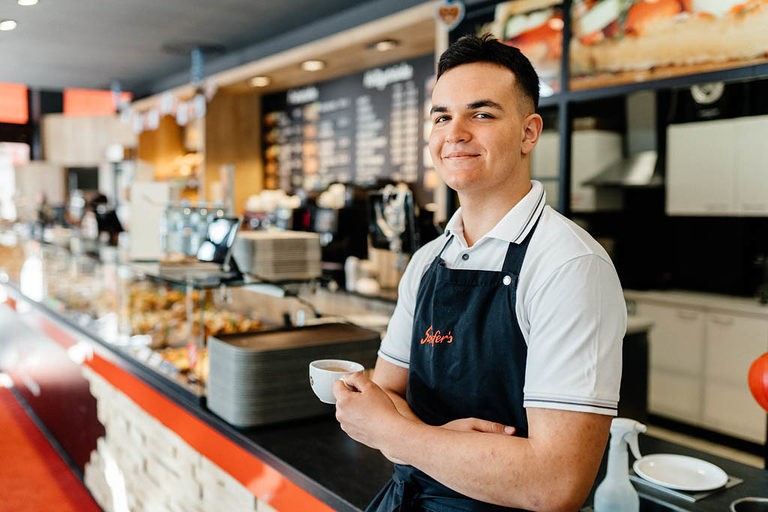 Ein Verkäufer-Azubi posiert am Tresen in einem Cafè