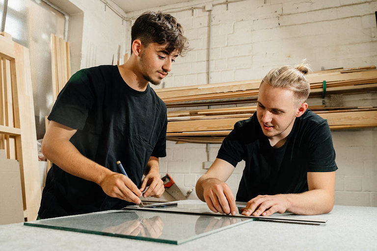 Zwei Glaser-Azubis arbeiten an einem Tisch in der Werkstatt