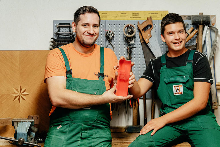 Zwei Parkettleger-Azubis posieren vor der Werkzeugwand.