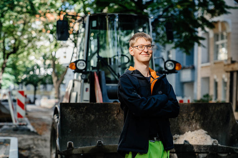 Ein Straßenbauer-Azubi posiert vor einem Bagger.