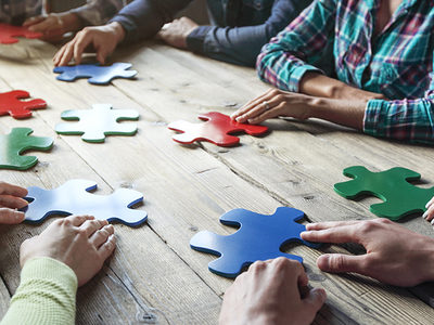 Viele Hände mit bunten Puzzleteilen an einem Tisch