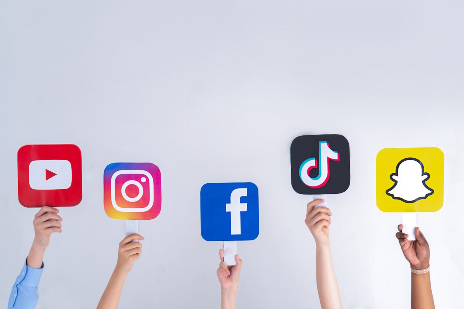Jugendliche halten Social-Media-Zeichen in ihren Händen: Youtube, Snapchat, Instagram, Tiktok, Facebook. 