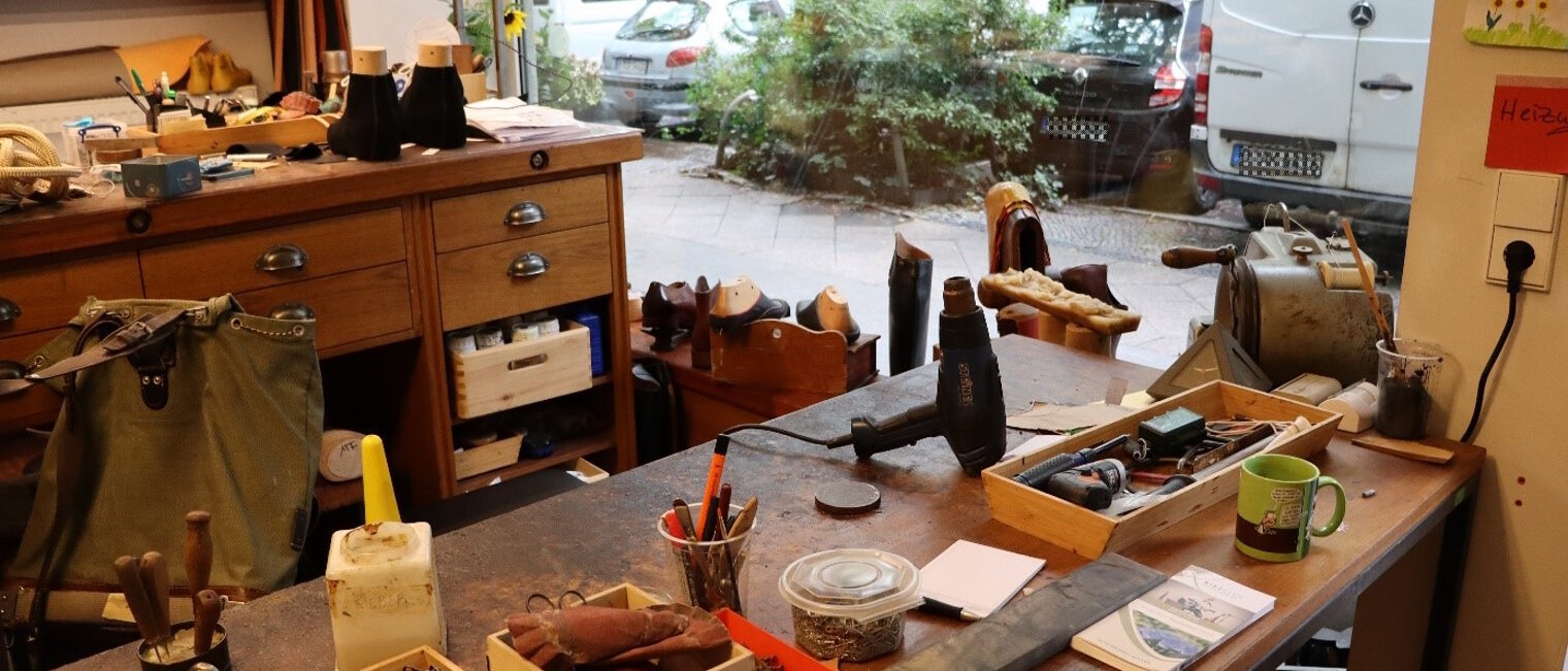 Blick von einer Orthop&auml;dieschumacher Werkstatt mit Werkb&auml;nken und Werkzeugen raus aus einem gro&szlig;en Schaufenster auf den B&uuml;rgersteig.