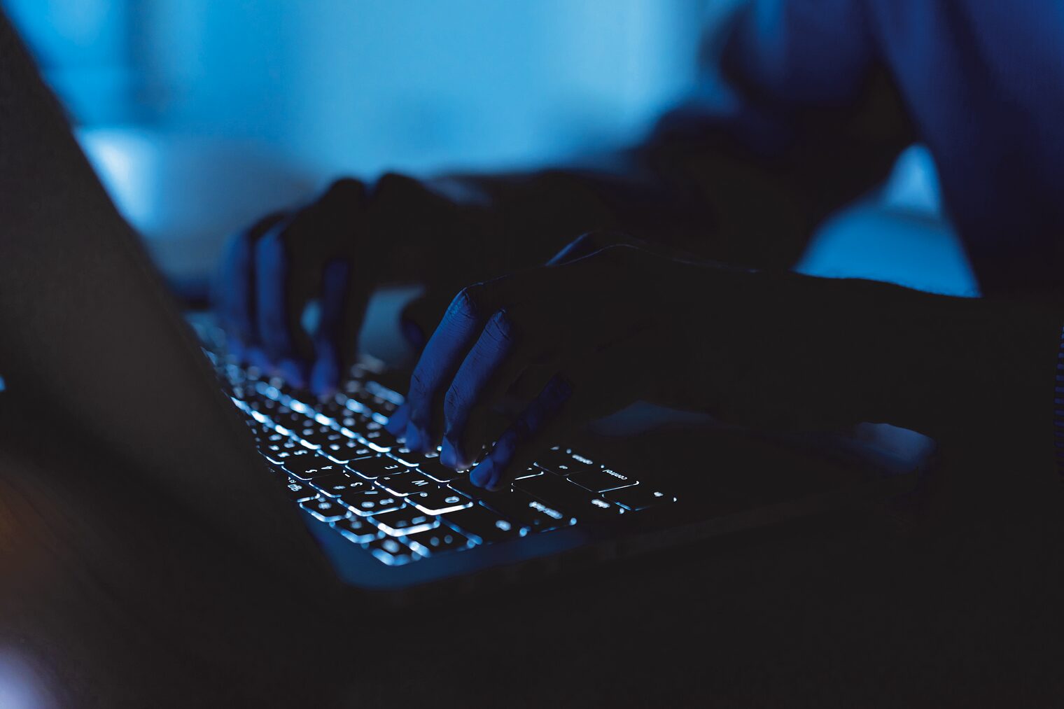 Symbolbild: Cyber-Angriff: Hände an einem Laptop in einem abgedunkelten Raum