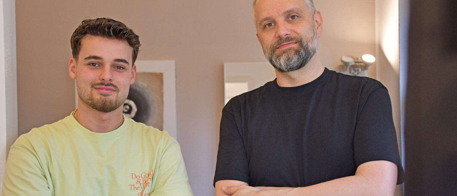 Rigers Bici und Georg Elfinger stehen in einem Friseursalon und lächeln in die Kamera