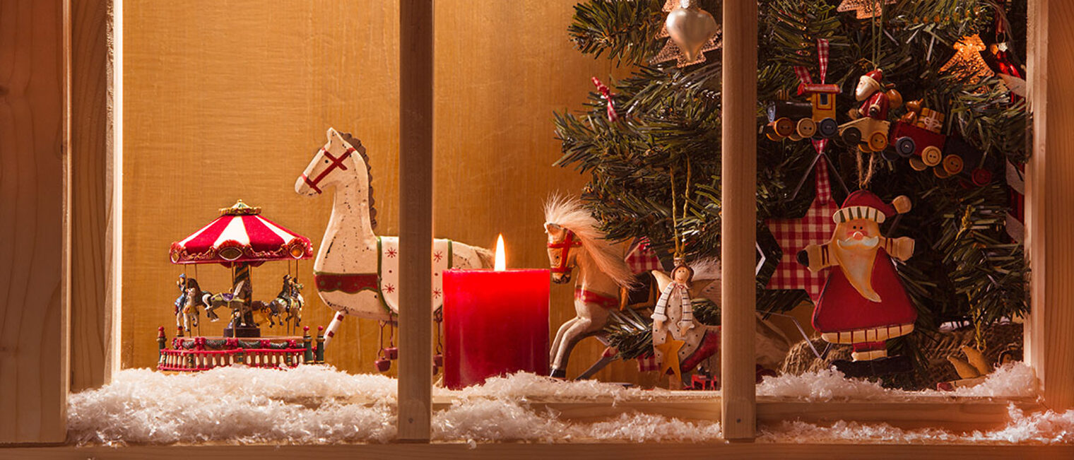 Weihnachtlich geschmücktes Fenster mit Schnee im Vordergrund und einem geschmückten Weihnachtsbaum.