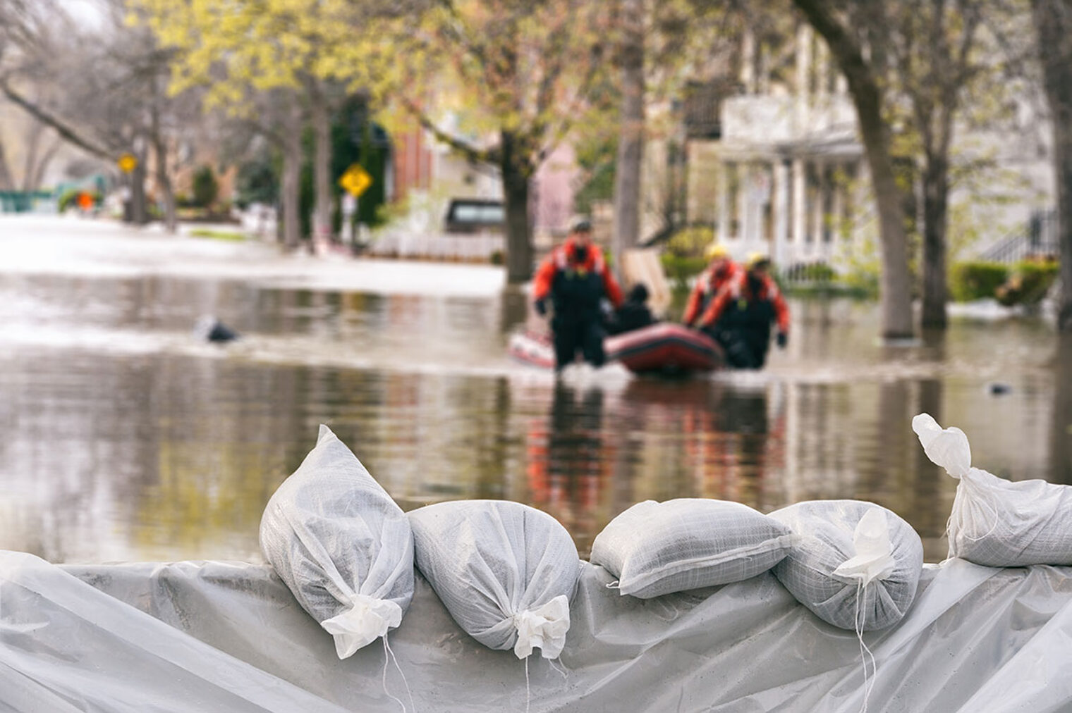 Überschwemmung in einer Stadt mit Sandsäcken und einem Rettungsboot und Helfer*innen.
