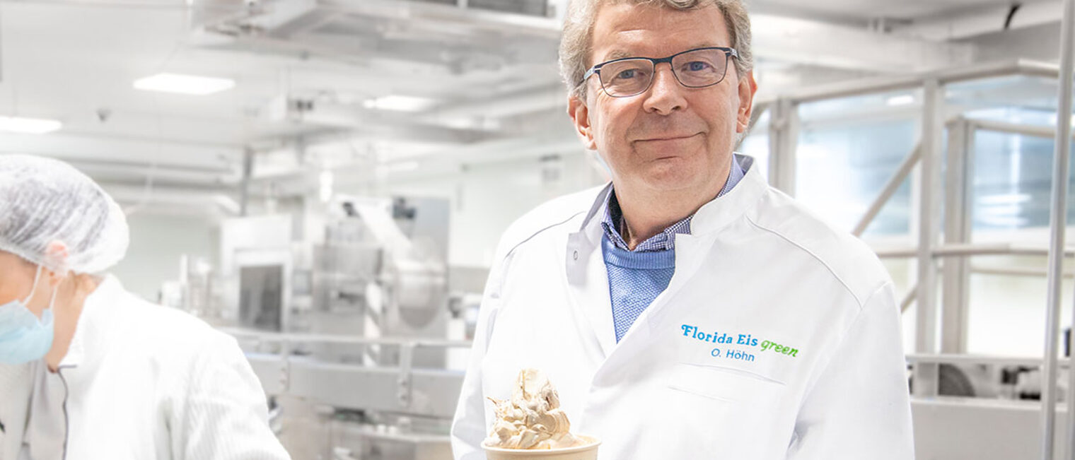 Olaf Höhn, der Geschäftsführer von Florida Eis, steht in der Produktion von Florida Eis mit einem Becher Eis in der Hand und lächelt in die Kamera.