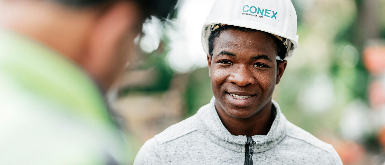 Portraitaufnahme eines lächelnden Stahlbetonbauerazubis im weißen Schutzhelm