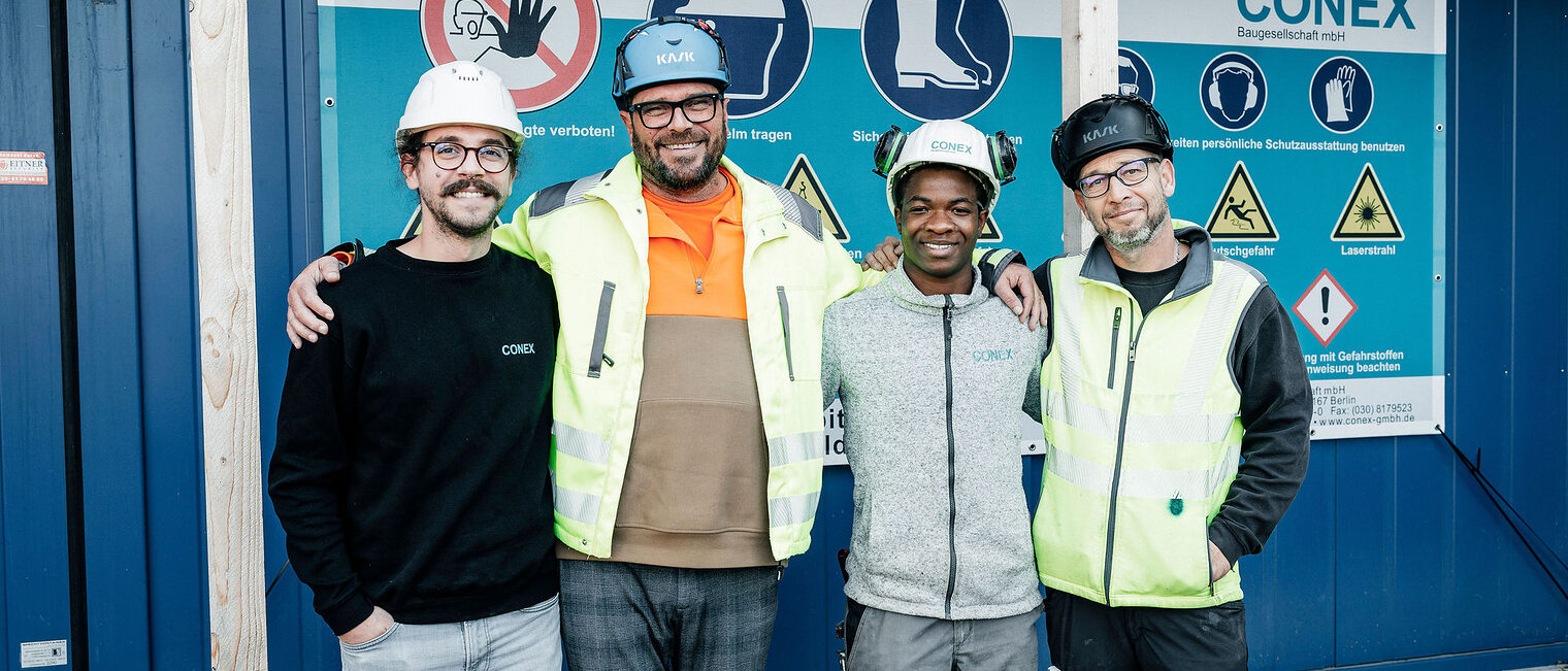 Vier Stahlbetonbauer posieren lächelnd vor der Kamera