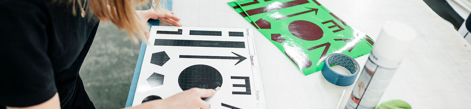 Eine Lichtreklameherstellerin entgittert schwarze Schriftelemente auf einer weißen Trägerfolie für eine Folienbeschriftung.