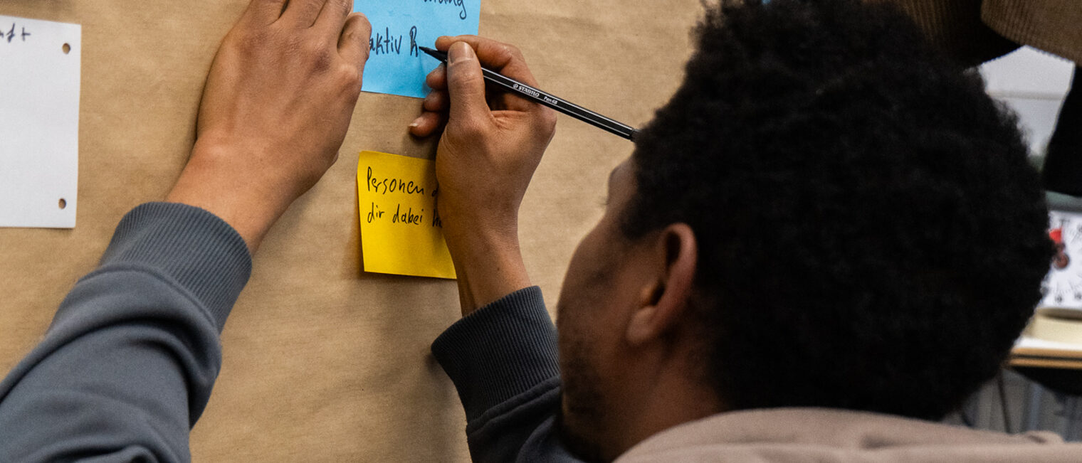 Blick von hinten: Ein Teilnehmer des Azubiwohnen-Workshops der Handwerkskammer Berlin klebt einen Zettel an die Tafel