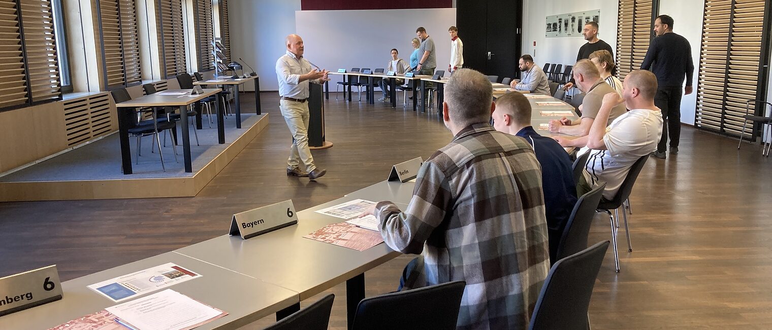 Azubis zu Besuch im Bundesrat: sie sitzen an einem langen Tisch und hören dem Redner zu.