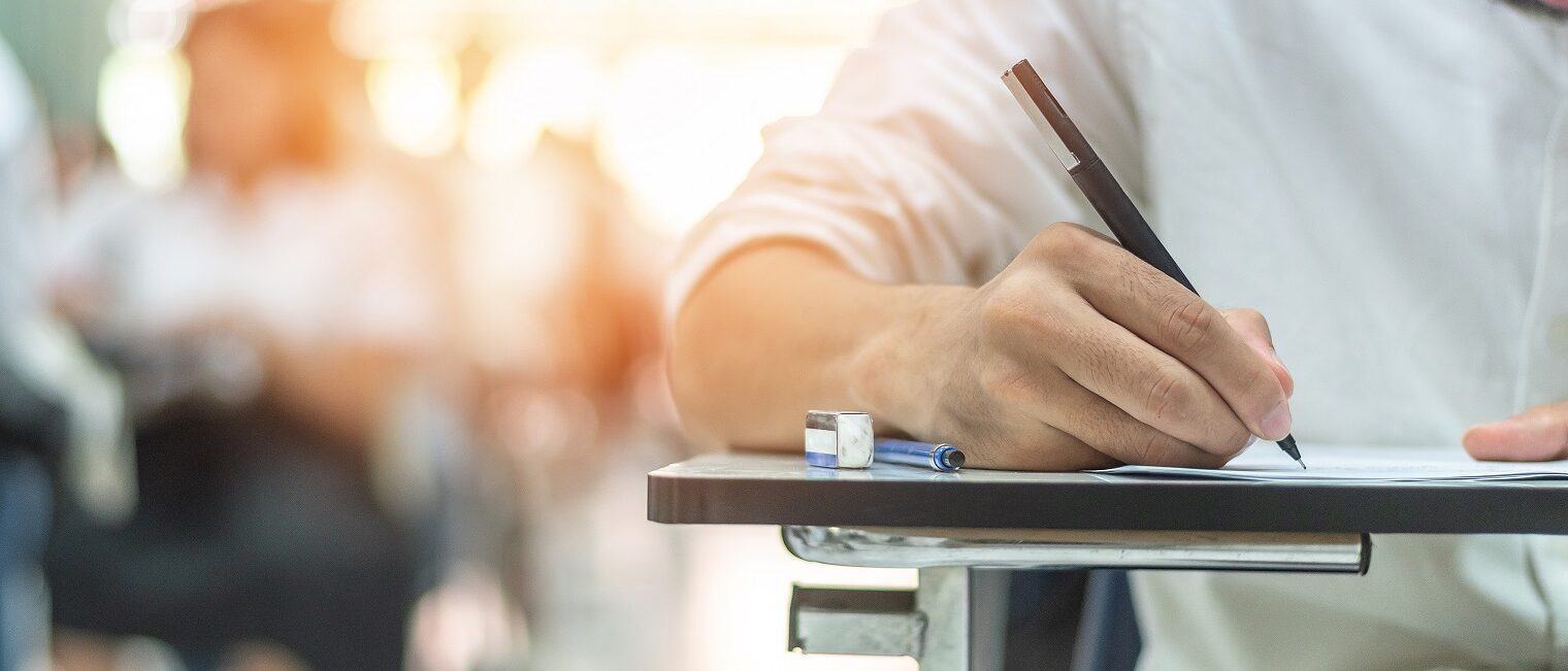 Schulprüfung, Detailaufnahme, Hand mit Stift an einer Unterlage: Schüler/in nimmt an einem Aufnahmetest im Klassenzimmer teil