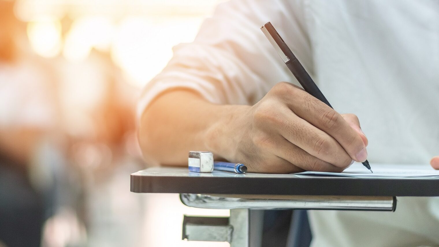 Schulprüfung, Detailaufnahme, Hand mit Stift an einer Unterlage: Schüler/in nimmt an einem Aufnahmetest im Klassenzimmer teil