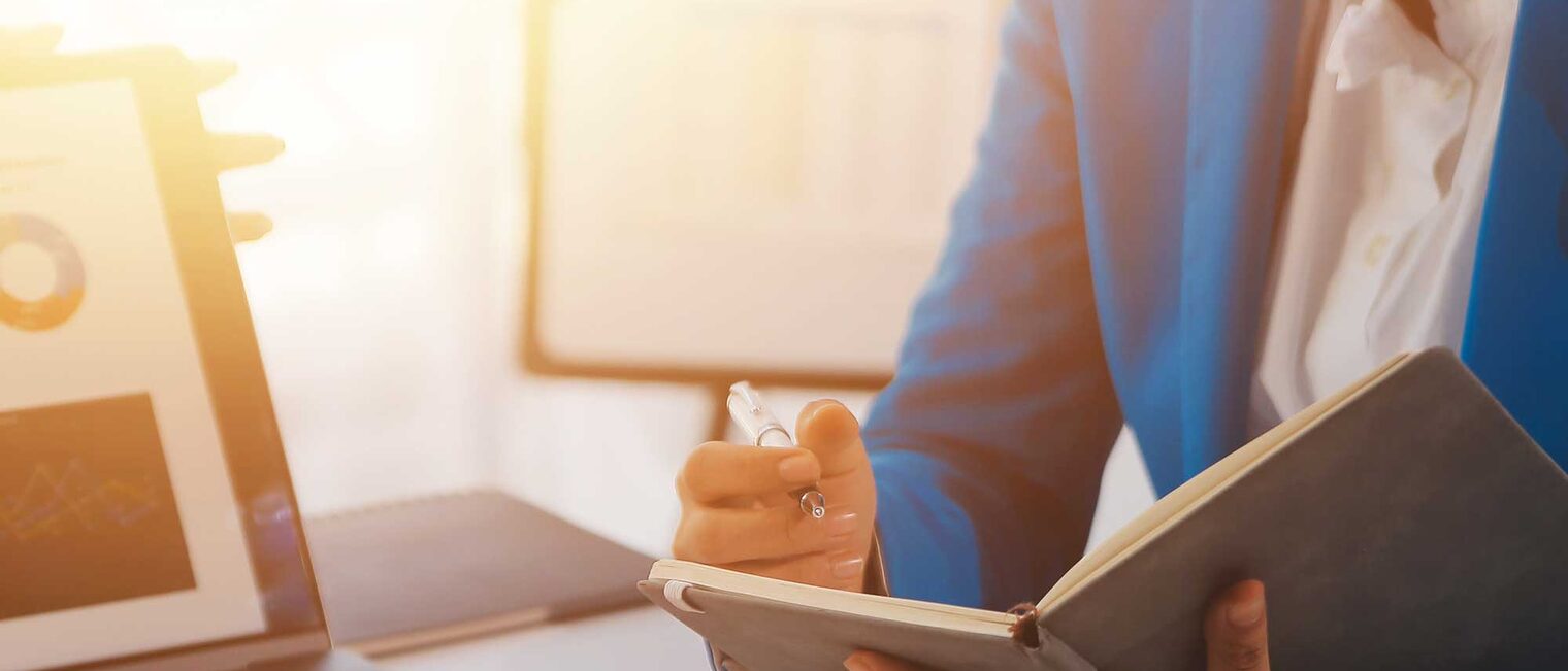 Eine Person sitzt an einem Schreibtisch mit einem geöffneten Notizbuch und ist in einem Beratungsgespräch.