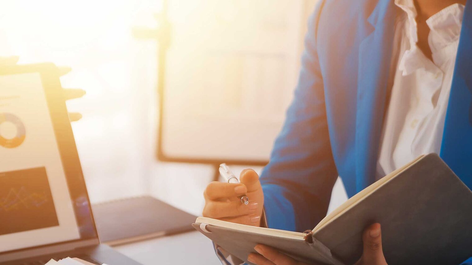 Eine Person sitzt an einem Schreibtisch mit einem geöffneten Notizbuch und ist in einem Beratungsgespräch.