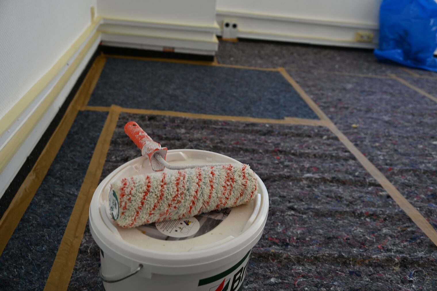 Farbeimer mit Malerwalze auf dem Teppichboden