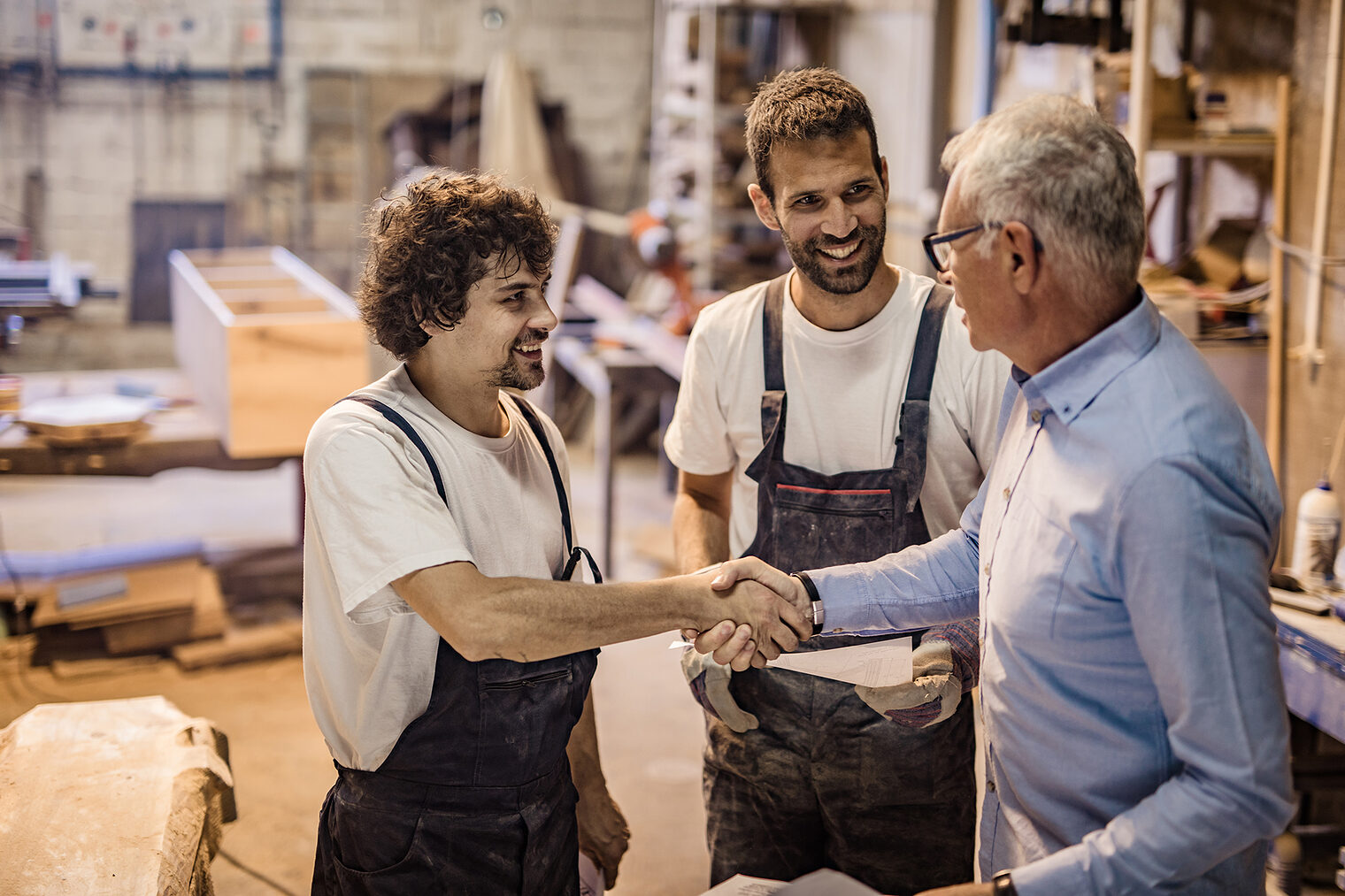 Zwei Mitarbeiter eines Handwerksbetriebs unterhalten sich auf einer Baustelle mit einem Kunden und schütteln ihre Hände.