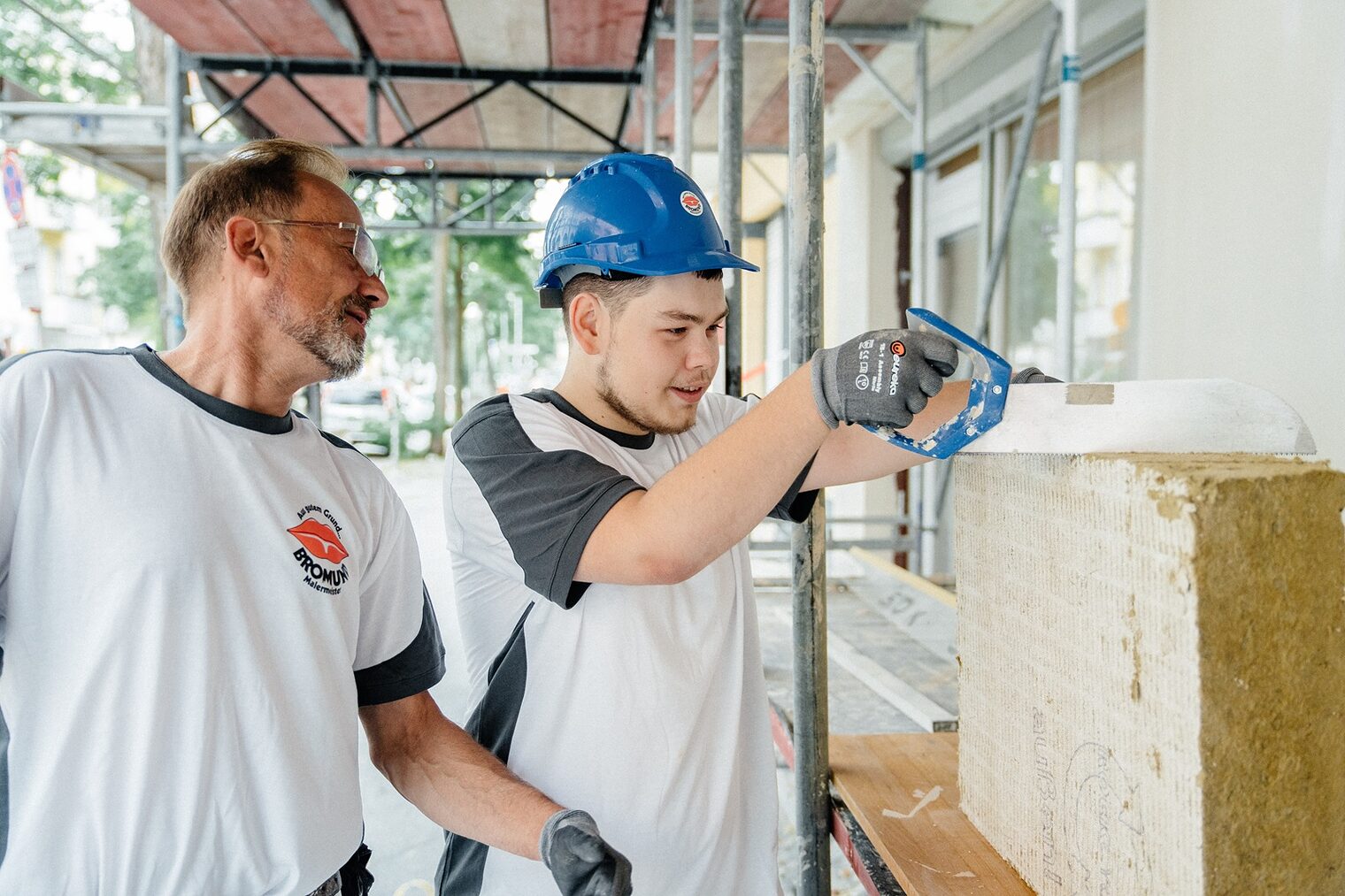 Maler-Azubi und sein Meister beim Arbeiten an einer Hausfassade