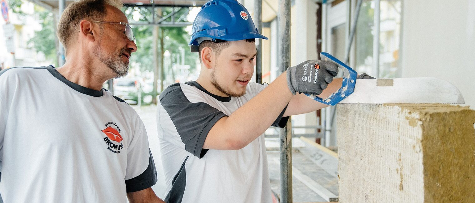 Maler-Azubi und sein Meister beim Arbeiten an einer Hausfassade