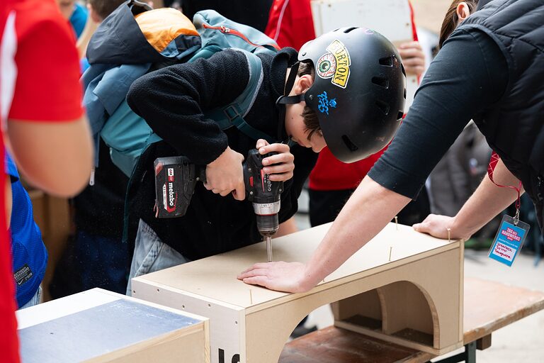 Ein Junge mit Schutzhelm bohrt an einer Fingerboardrampe aus Holz am Tag des Handwerks im Berliner Mellowpark am 19.09.2026.