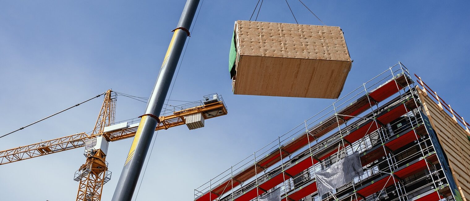Ein Kran hebt ein vorgefertigtes Holzbaumodul an seine Position im Bauwerk.