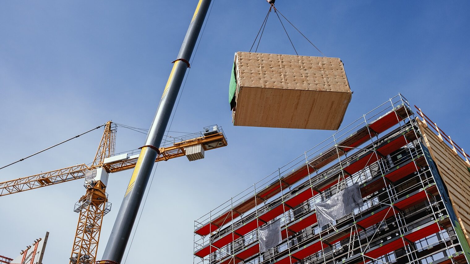 Ein Kran hebt ein vorgefertigtes Holzbaumodul an seine Position im Bauwerk.