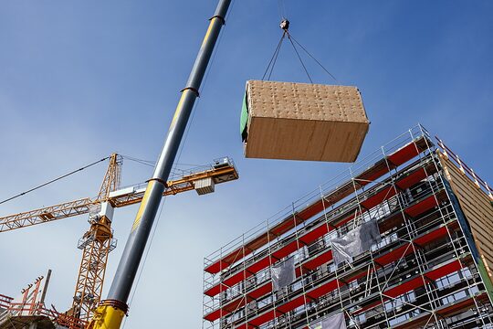 Ein Kran hebt ein vorgefertigtes Holzbaumodul an seine Position im Bauwerk.