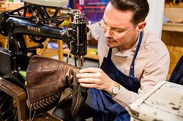 Schuster an der Nähmaschine mit einem Stiefel in der Hand